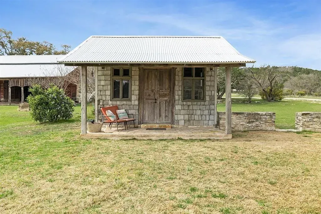 A small stone house with a white roof is sitting in the middle of a grassy field.