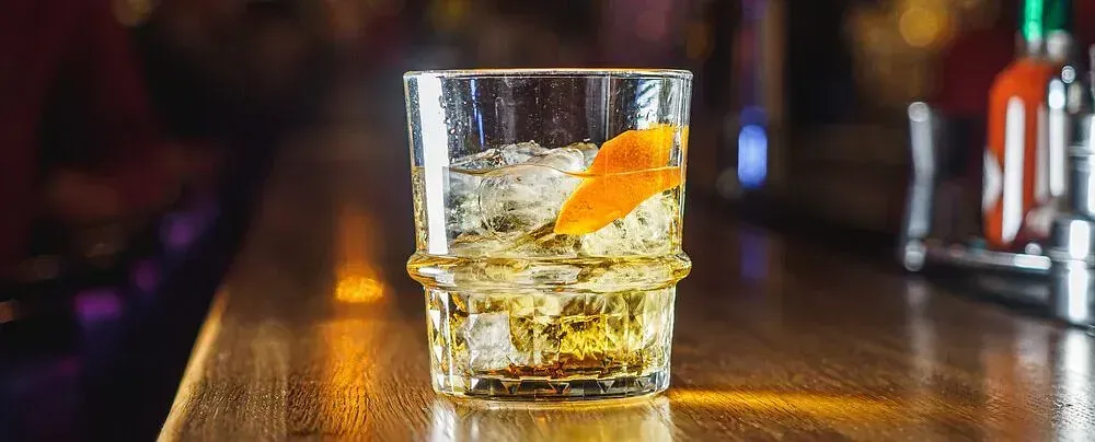 Un vaso de whisky con hielo y una cáscara de naranja en una barra.