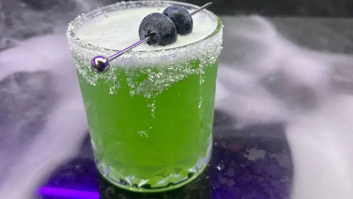 Una bebida verde con arándanos encima en un vaso sobre una mesa.