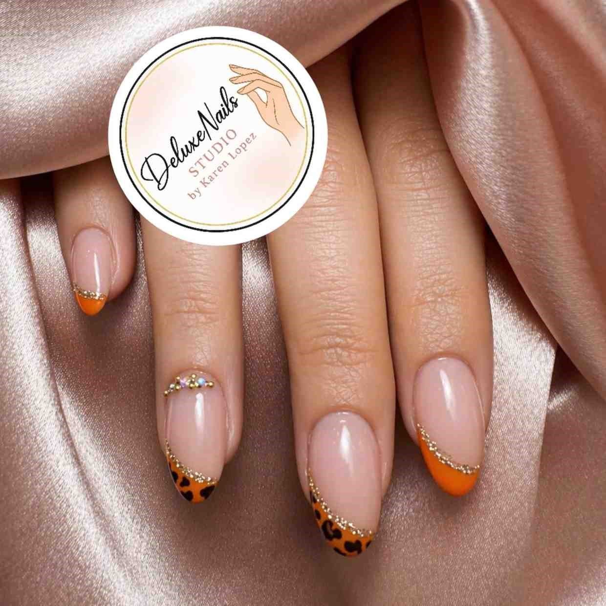 Manicura color nude con puntas francesas de estampado de leopardo naranja y detalles dorados en una mano.