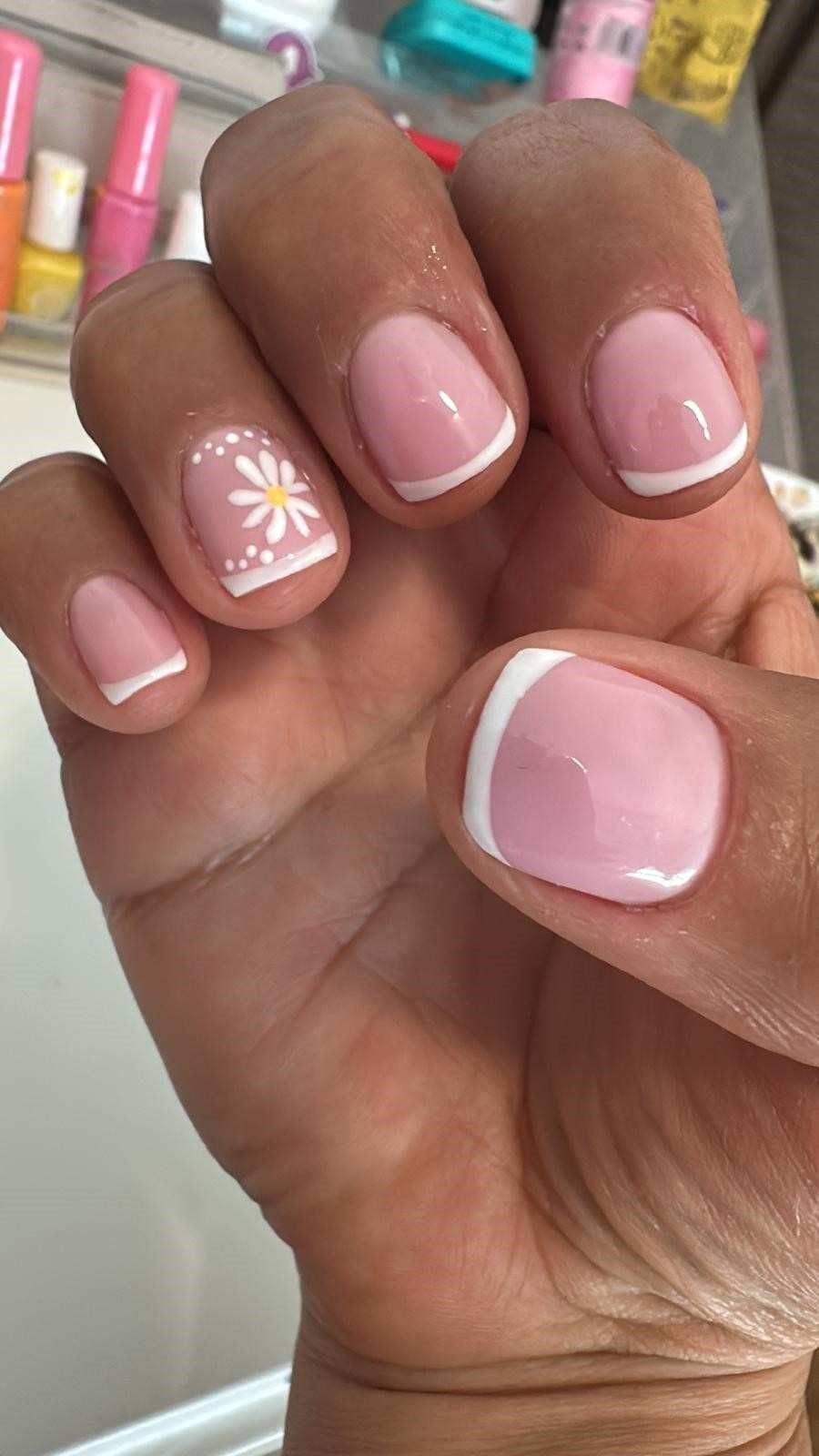 Mano con uñas de color rosa pálido con punta francesa y una pequeña flor blanca como adorno en una uña.