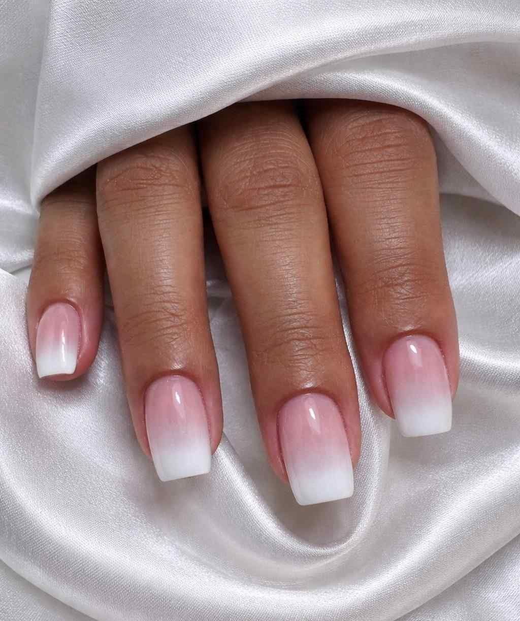 Mano con uñas francesas degradadas de rosa a blanco descansando sobre tela de satén blanca.