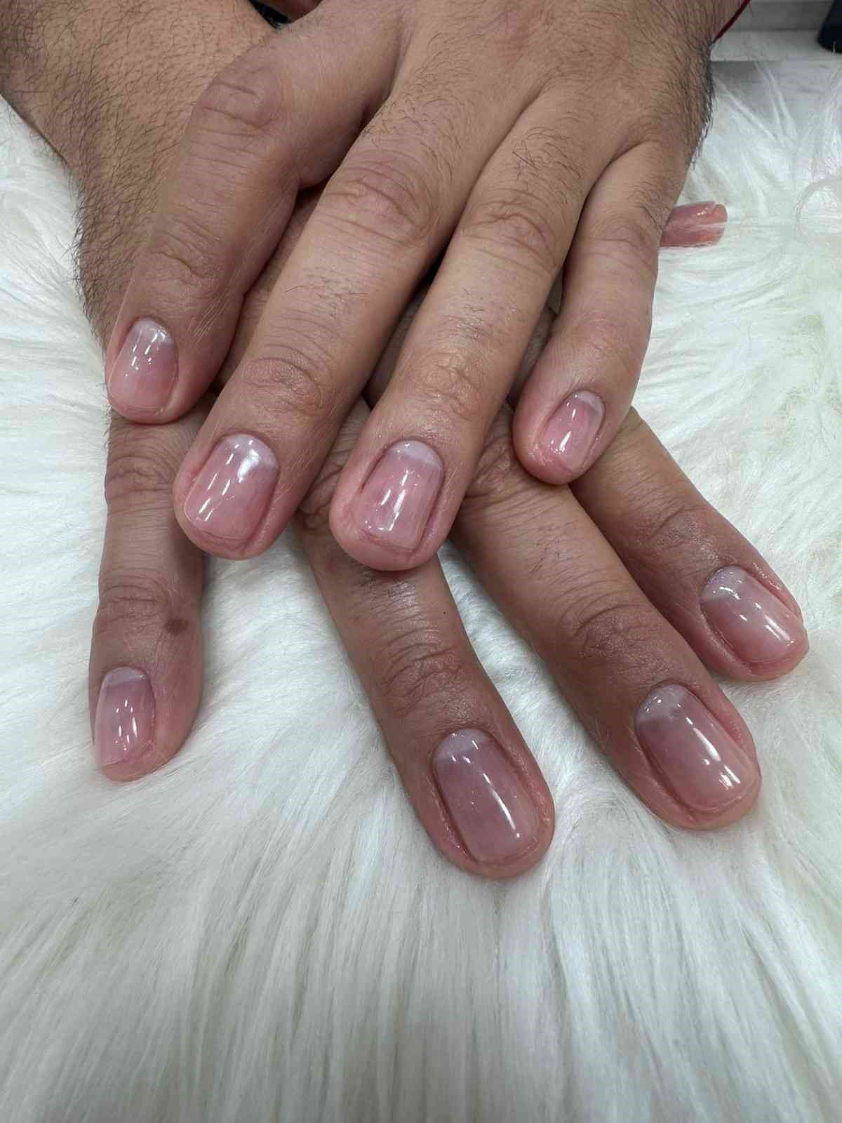 Primer plano de unas manos bien cuidadas con uñas rosas brillantes, que descansan sobre una superficie de piel blanca.