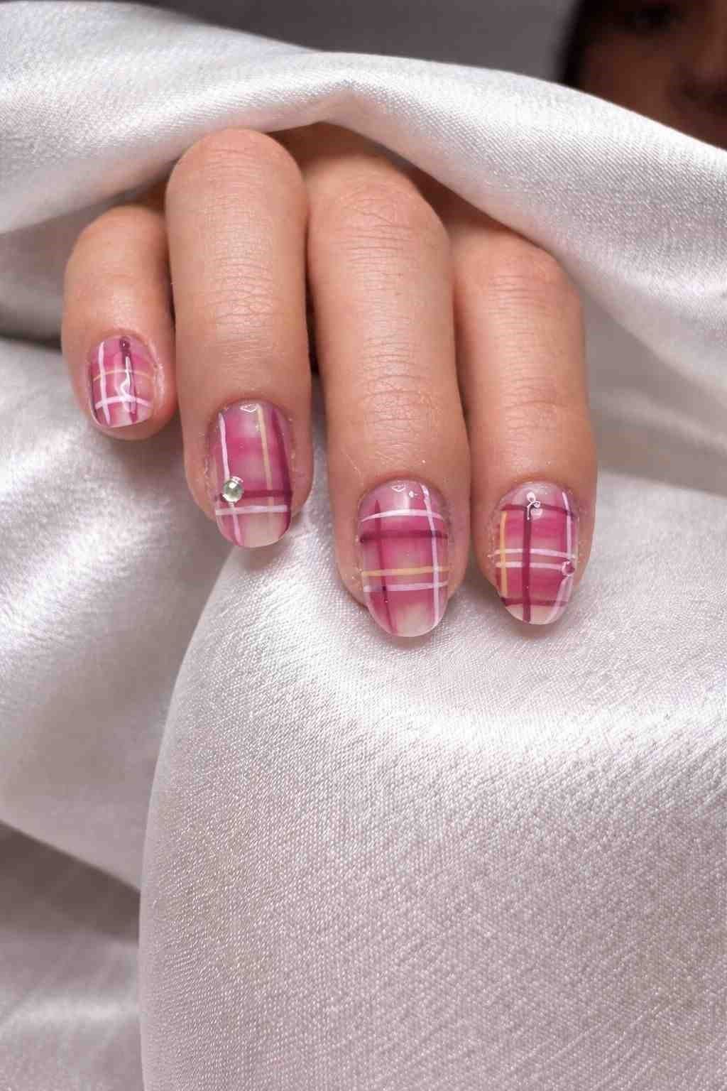 Mano con uñas decoradas con estampado de cuadros rosas sobre tela de satén blanca.