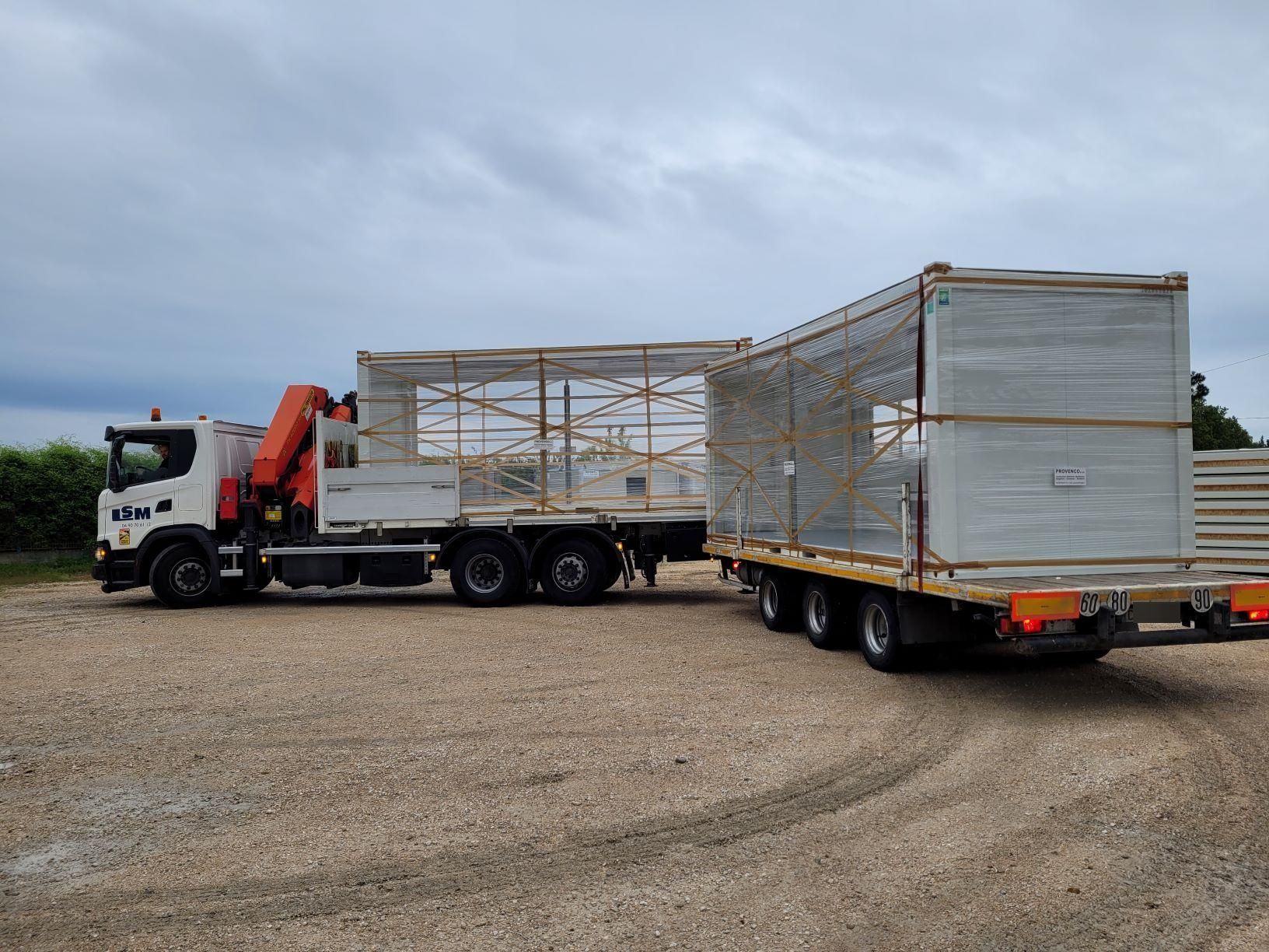Un semi-remorque blanc transporte une longue remorque bâchée sur un terrain gravillonné sous un ciel nuageux.