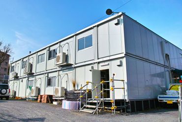 Bâtiment de bureaux modulaire avec murs blancs, fenêtres et petite échelle sur un terrain en gravier.
