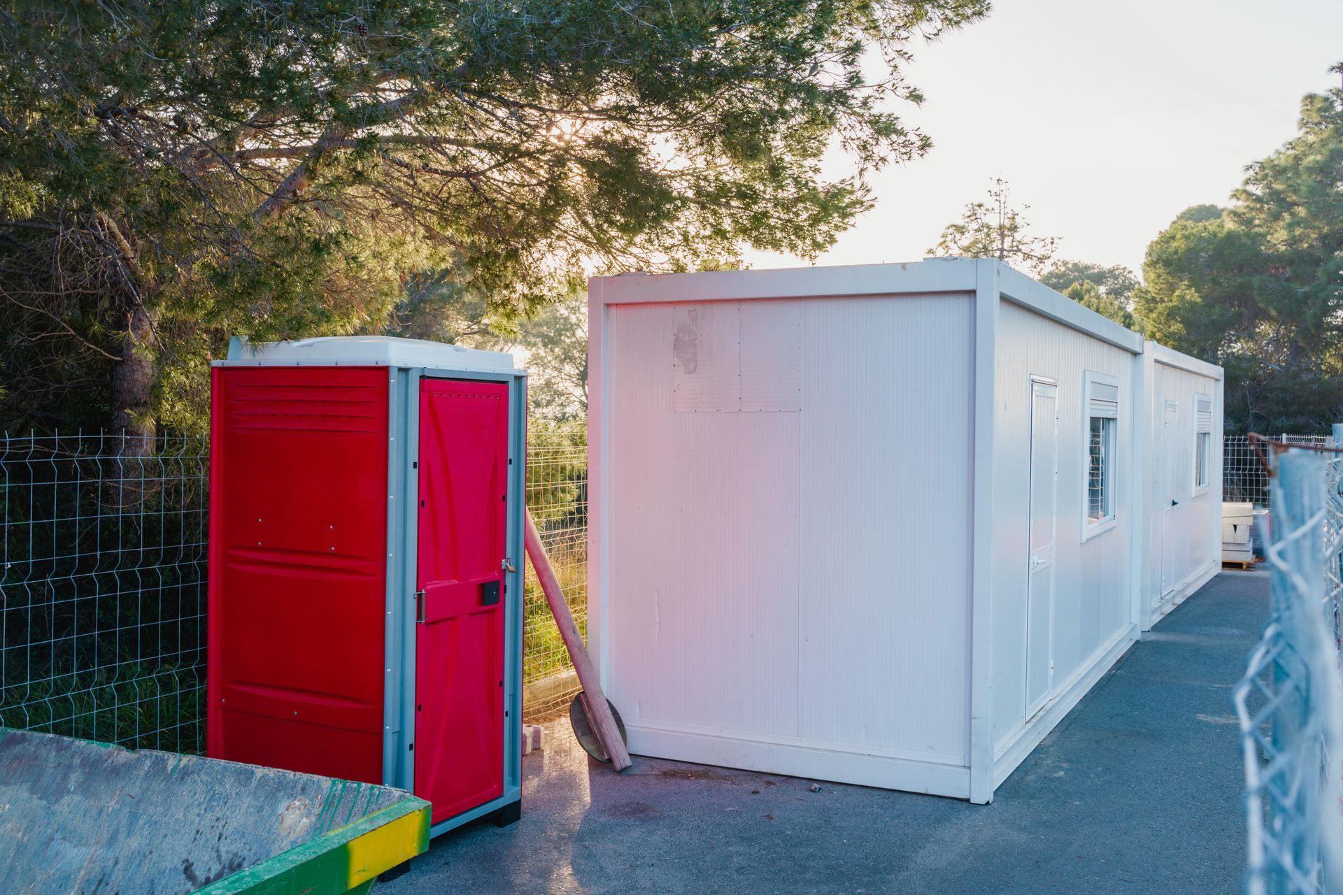 Toilettes portables rouges à côté d'un bâtiment portable blanc en bord de route au coucher du soleil.