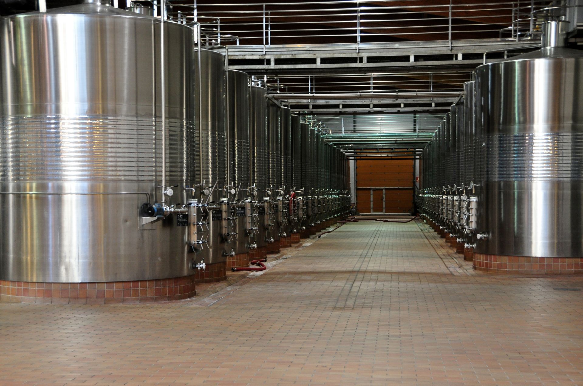 Des rangées de grandes cuves à vin en acier inoxydable dans un couloir de cave industrielle.