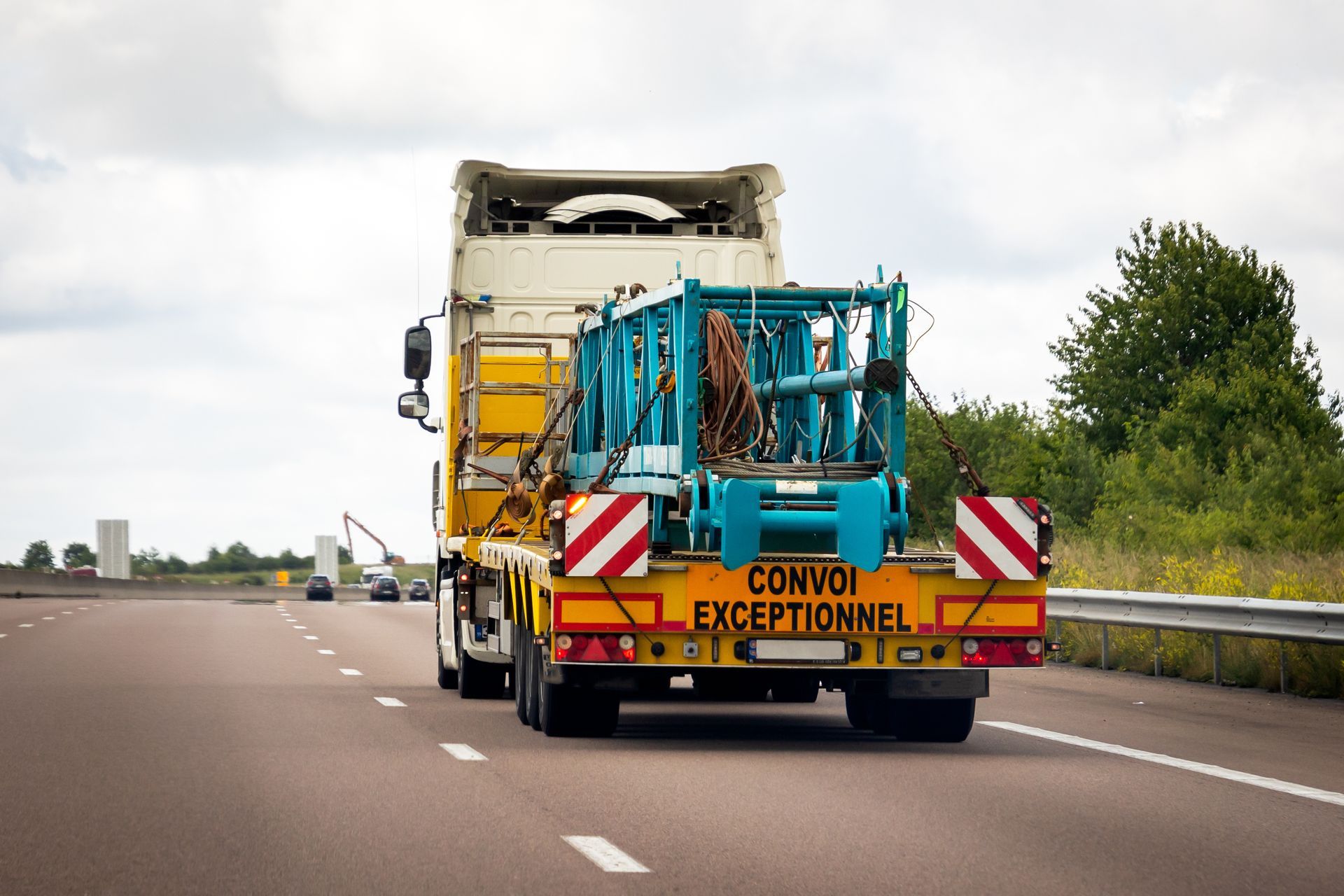 Camion hors gabarit transportant des engins jaunes et turquoise circulant sur une autoroute.