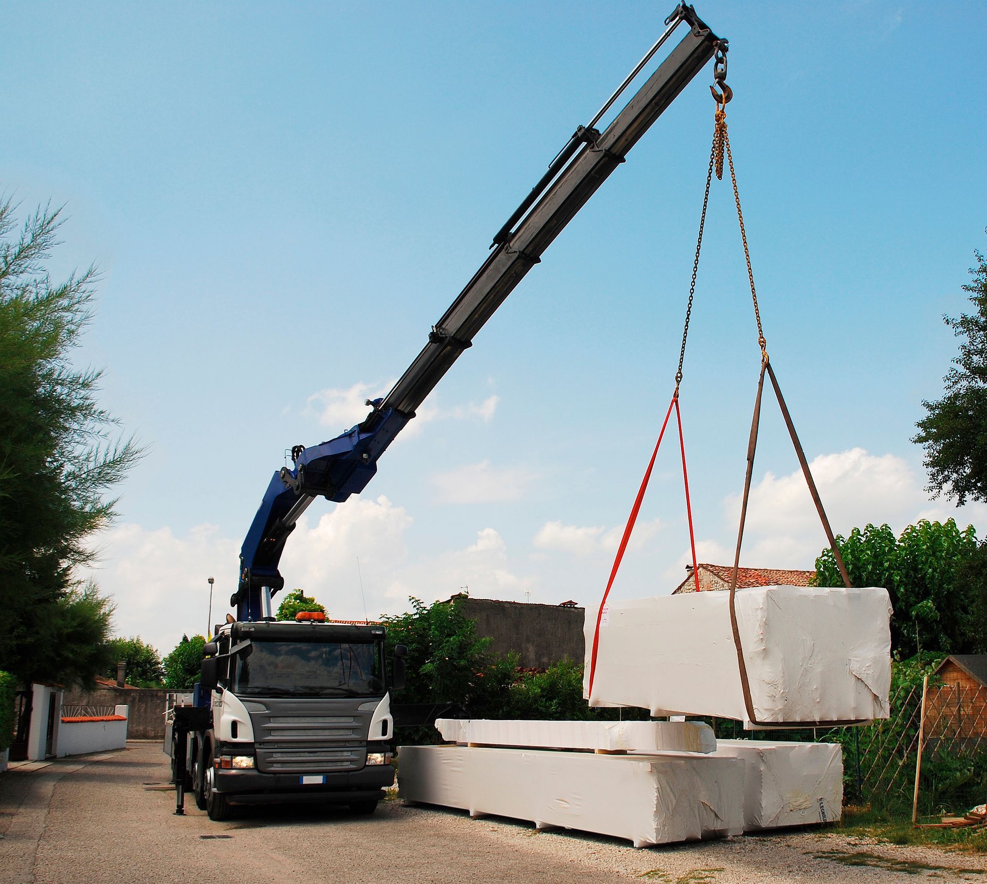 Camion-grue soulevant une grande dalle de béton blanc sur un chantier de construction.