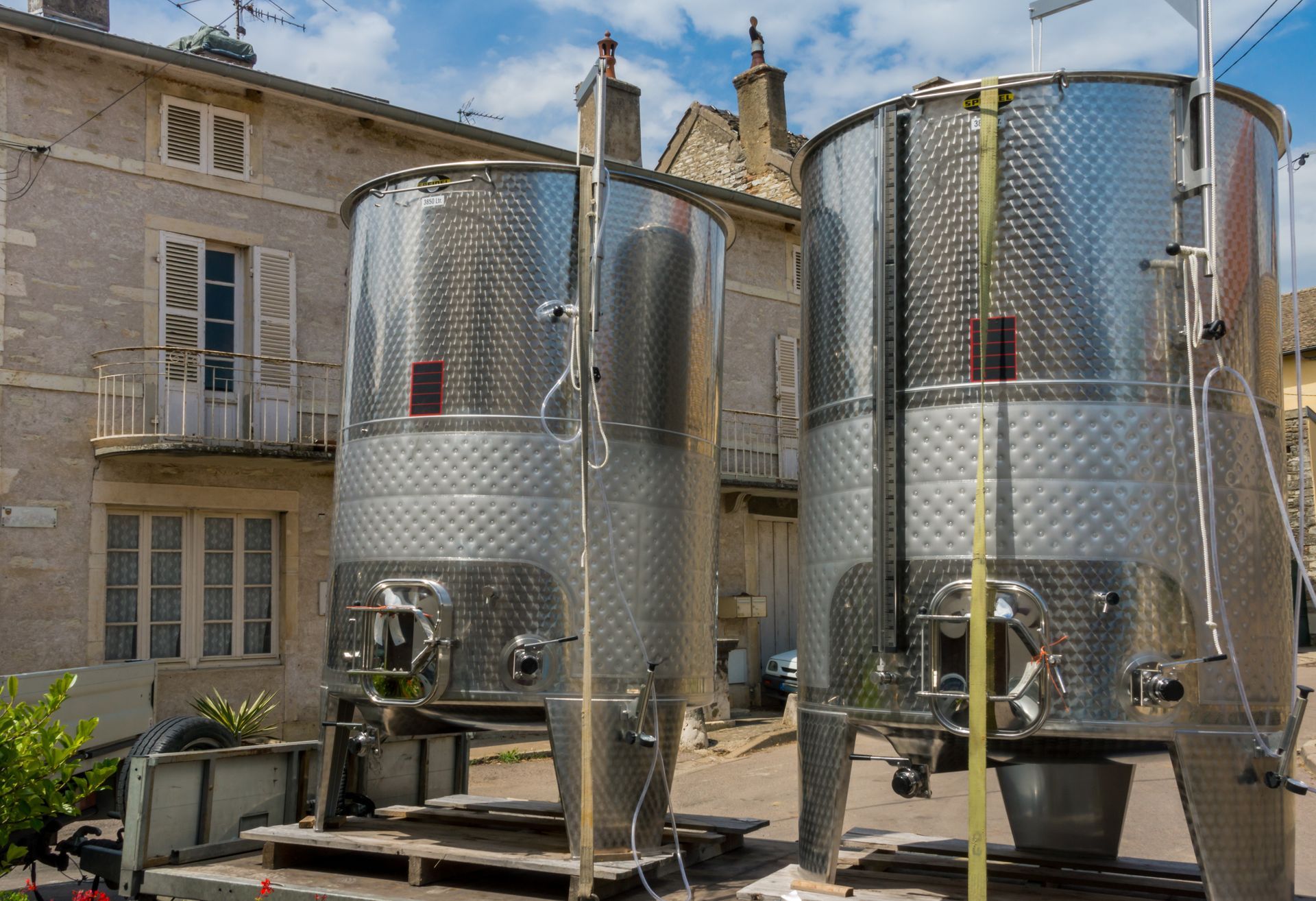 Deux grandes cuves de fermentation en acier inoxydable dans une cour à côté d'un bâtiment en pierre.
