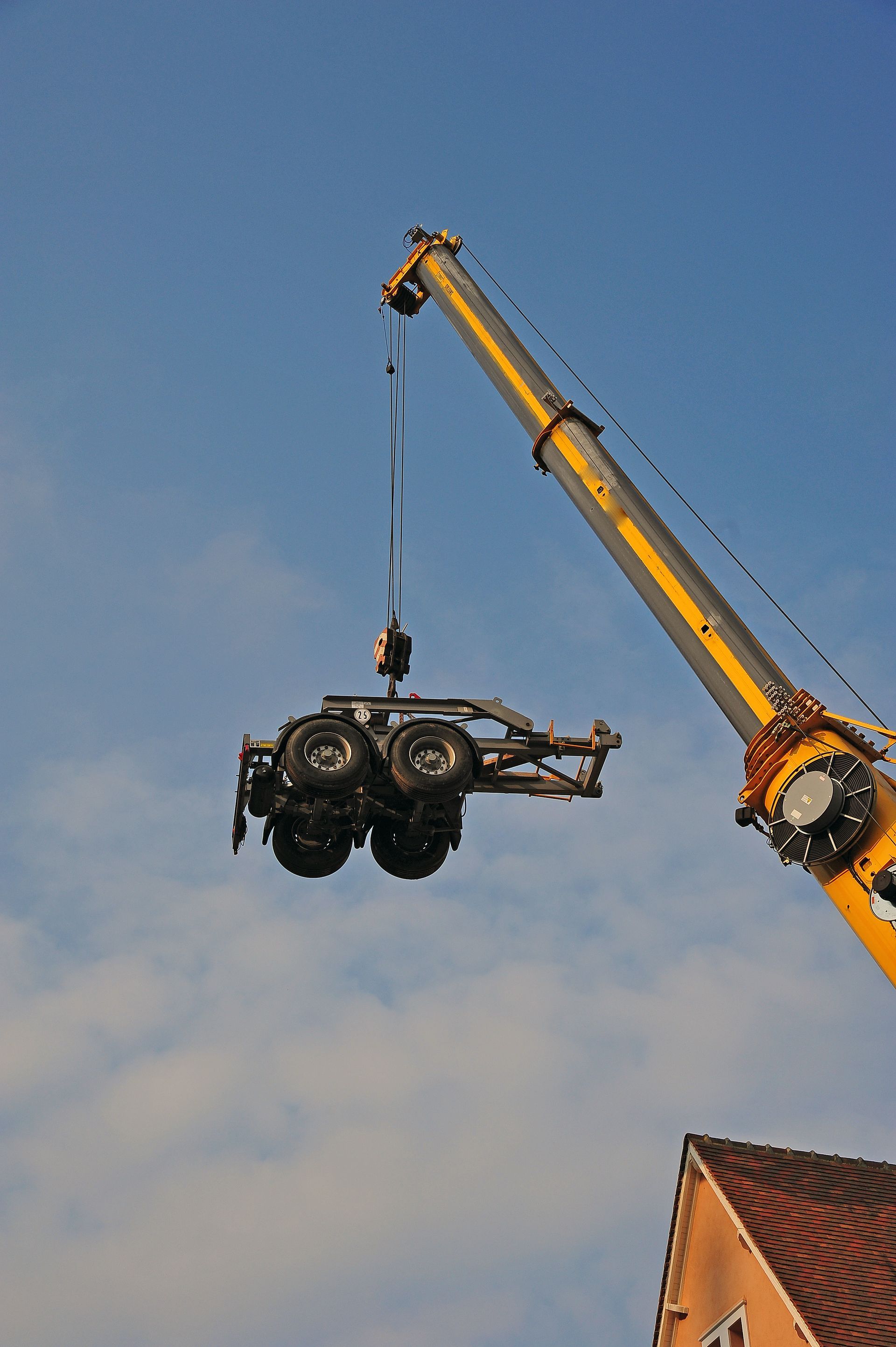 Une grue jaune soulève une voiture par des câbles sur fond de ciel bleu clair.