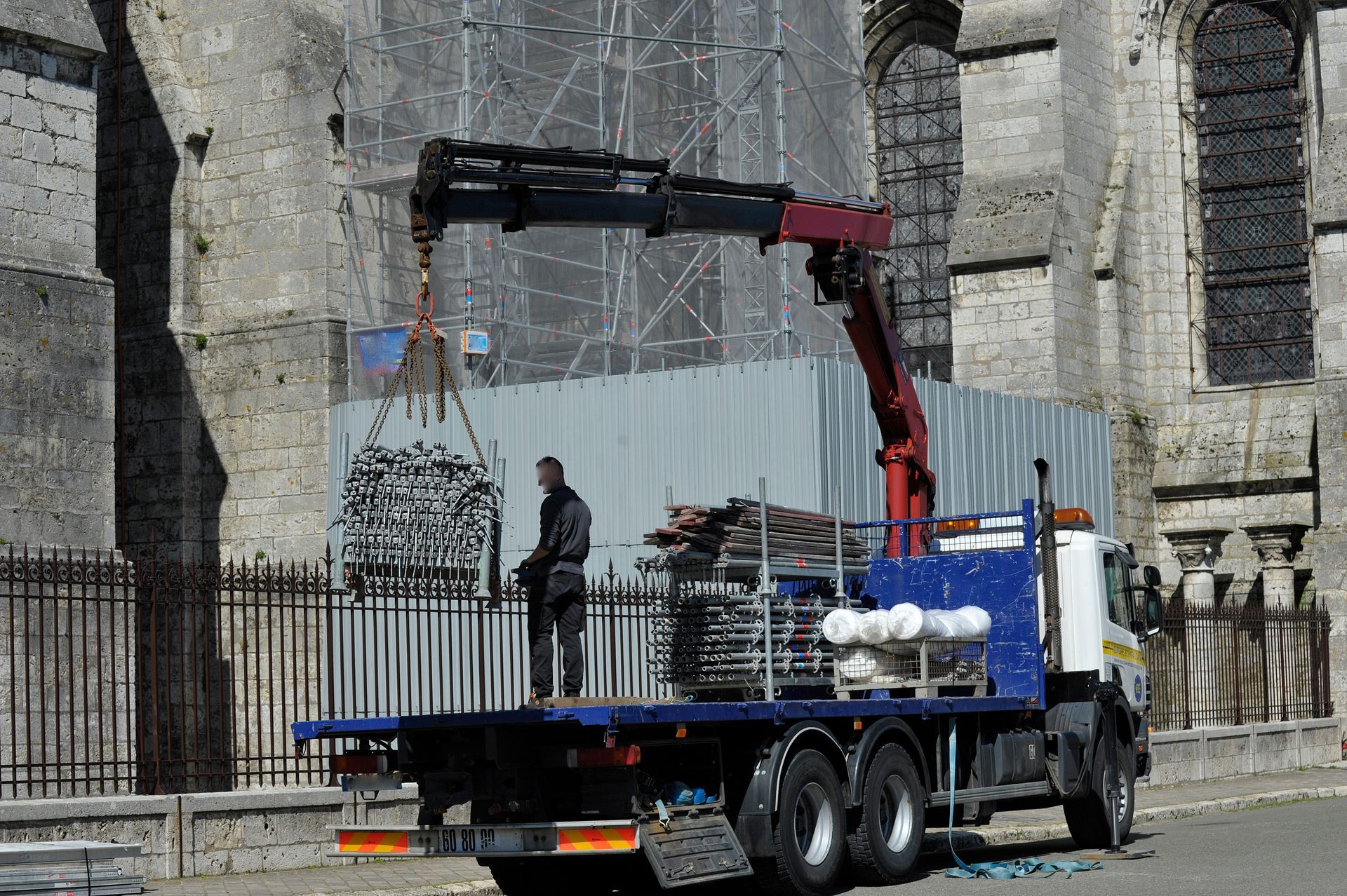 Camion-grue soulevant des débris près d'un mur de pierre, un ouvrier se tenant debout sur le plateau.