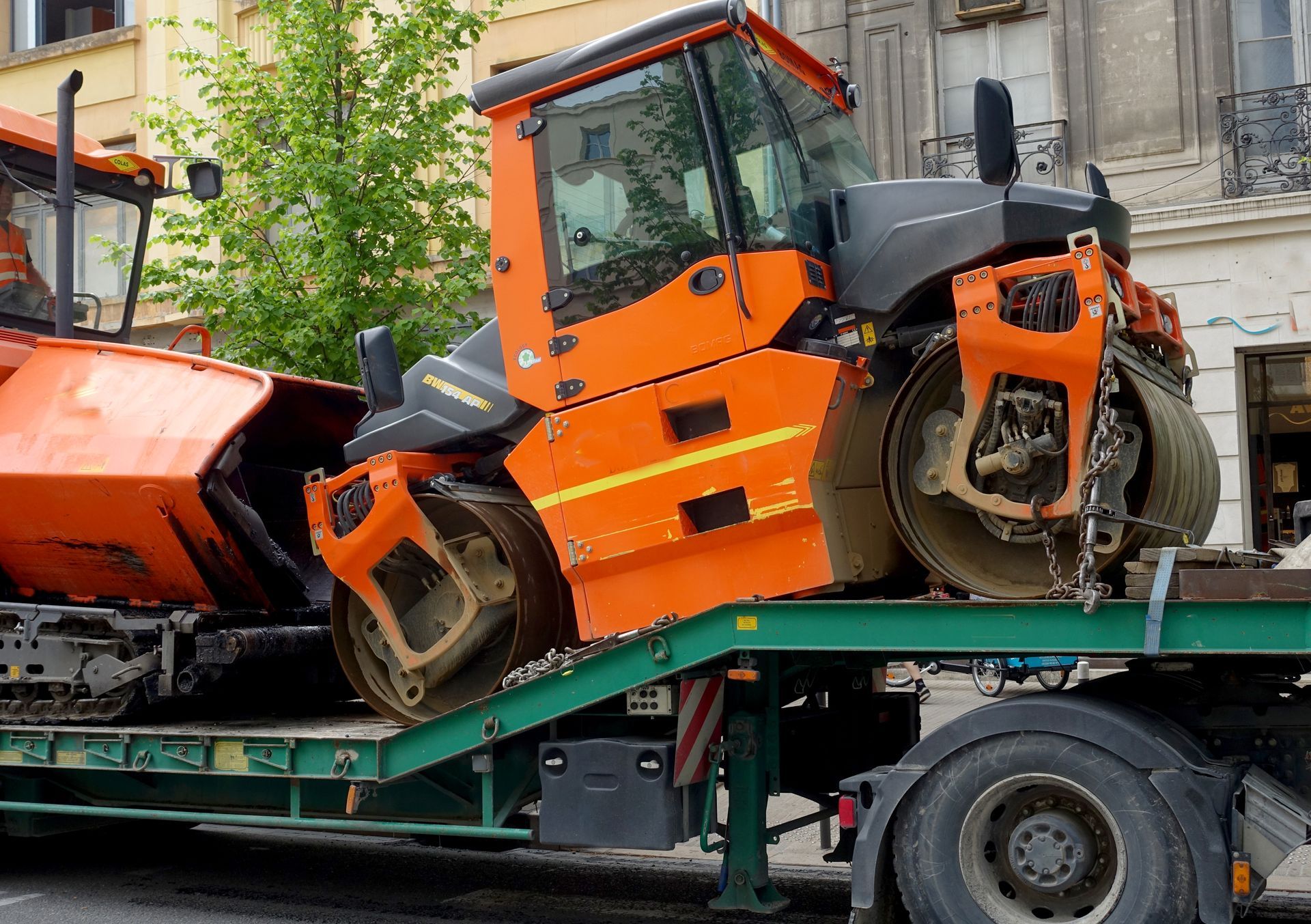 Deux rouleaux compresseurs orange chargés sur une remorque plate verte dans un environnement urbain.