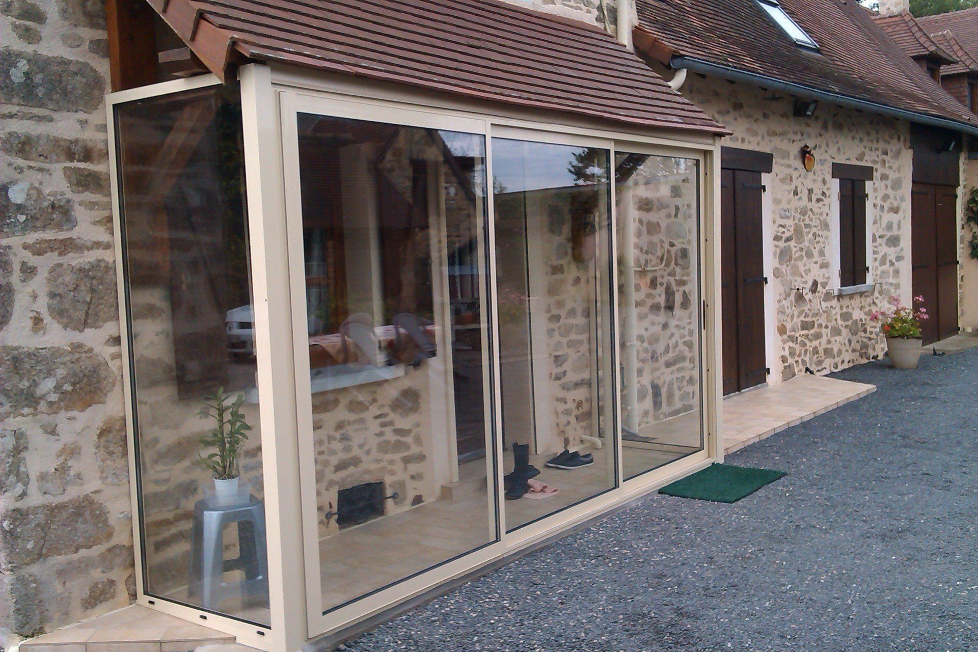 Patio vitré fermé, attenant à un bâtiment en pierre avec un toit de tuiles.