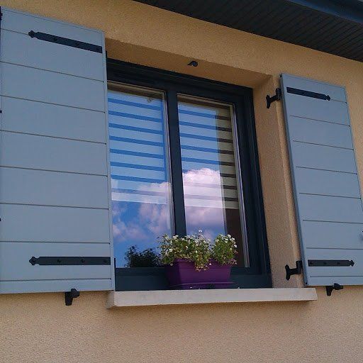 Volets gris à une fenêtre avec un pot de fleurs violet.