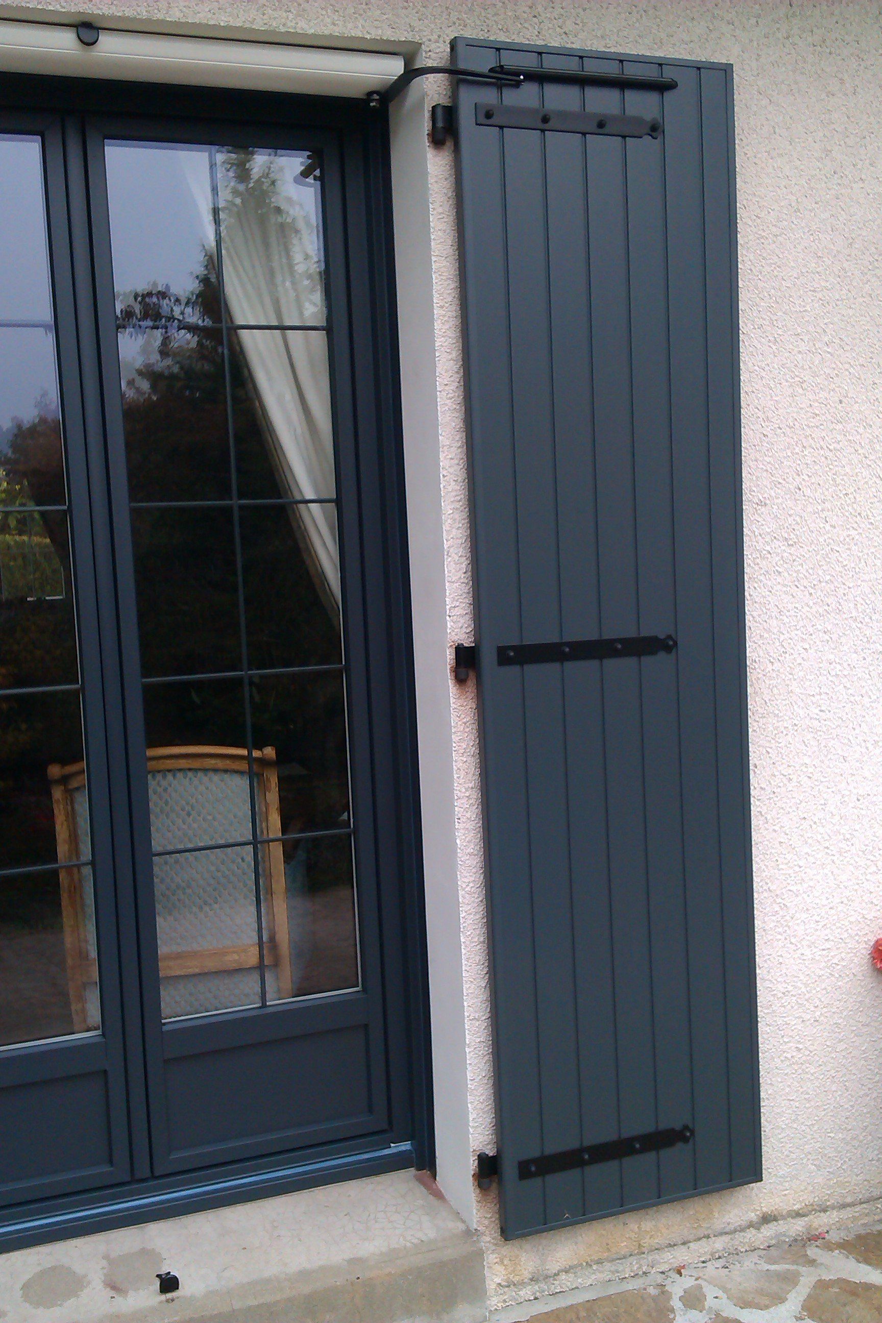 Volet gris foncé fermé à côté d'une porte vitrée.
