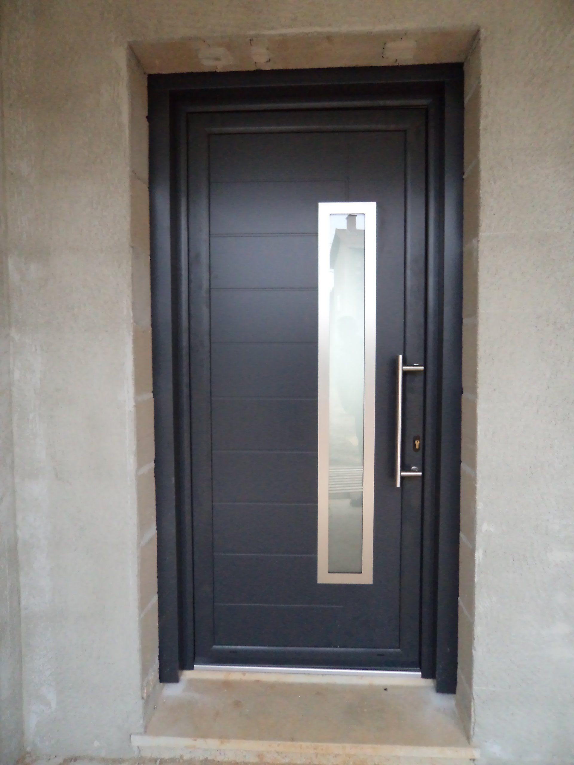 Porte d'entrée noire avec panneau vitré vertical et poignée argentée.