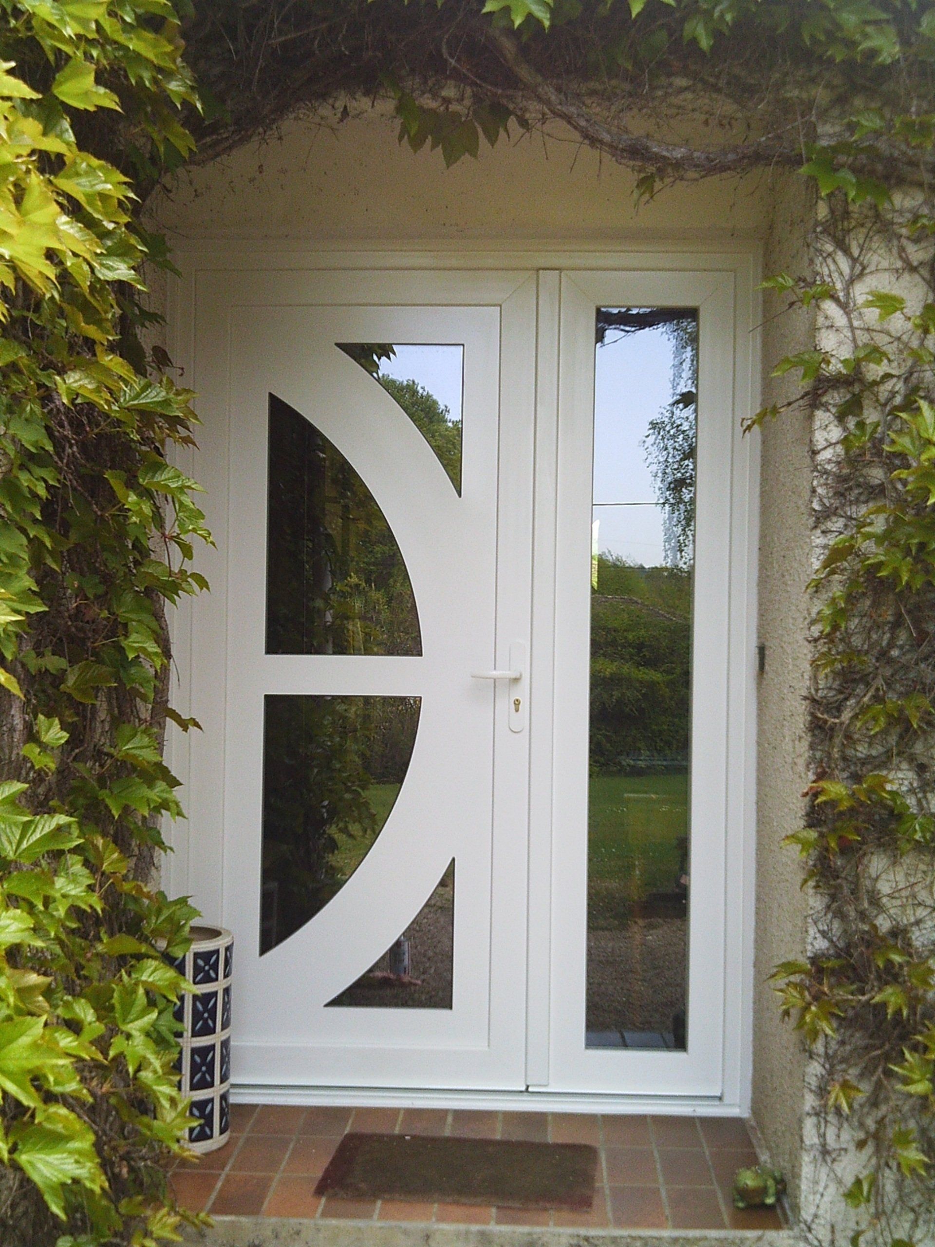Double porte blanche à panneaux de verre et au design incurvé, entourée de lierre.
