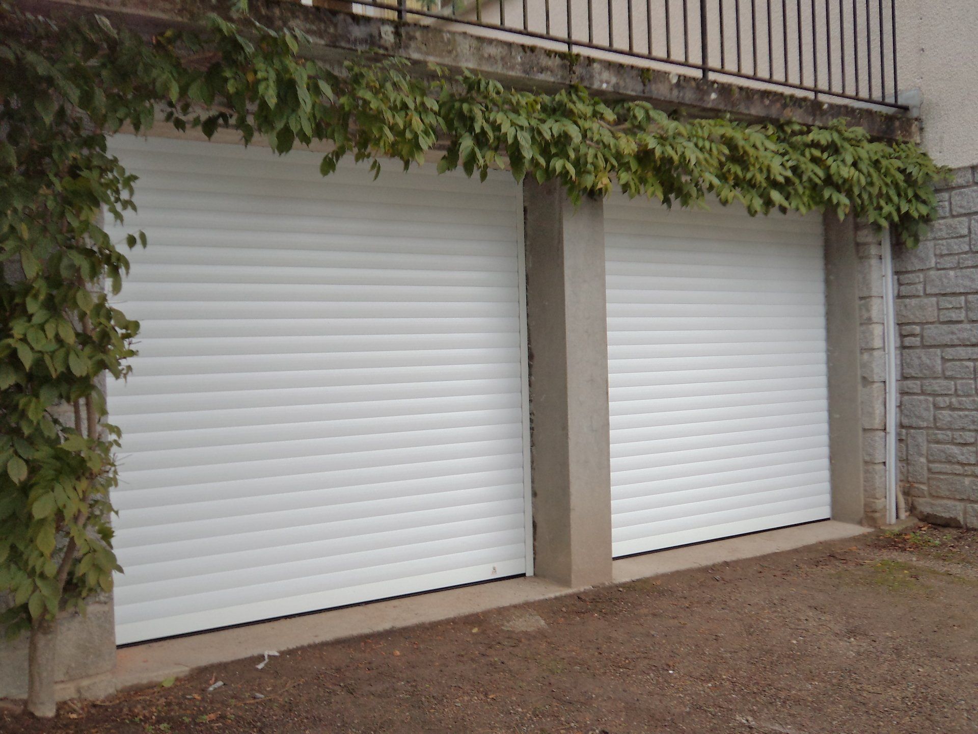 Deux portes de garage blanches fermées, recouvertes de vigne.