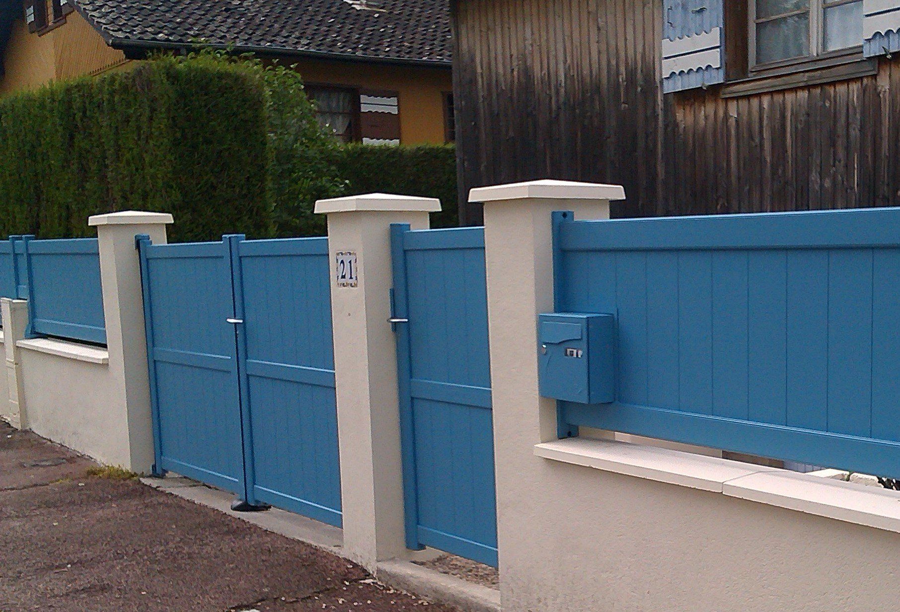 Portail et clôture bleus avec piliers blancs.