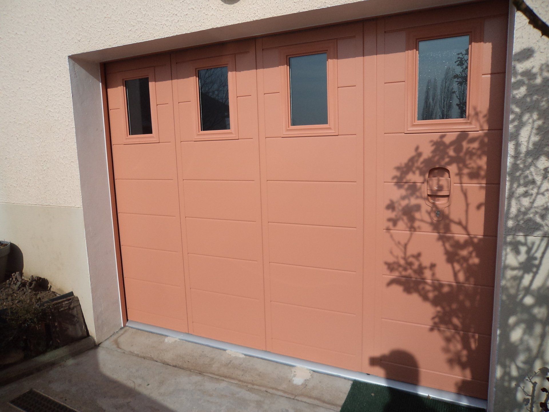 Porte de garage beige avec quatre petites fenêtres ; extérieur du bâtiment.