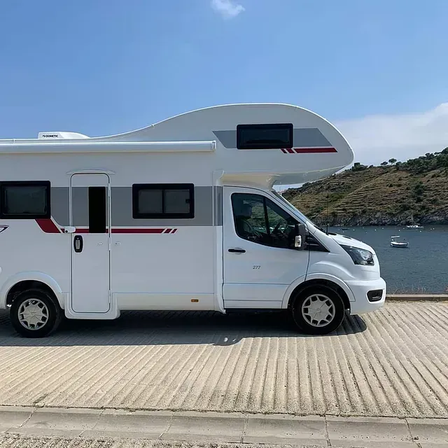 Una casa rodante blanca está estacionada al costado de la carretera junto a un cuerpo de agua.