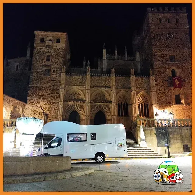 Una autocaravana está estacionada frente a un castillo por la noche.