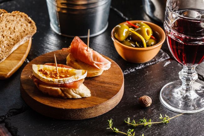 Una tabla de cortar de madera cubierta con comida y una copa de vino.