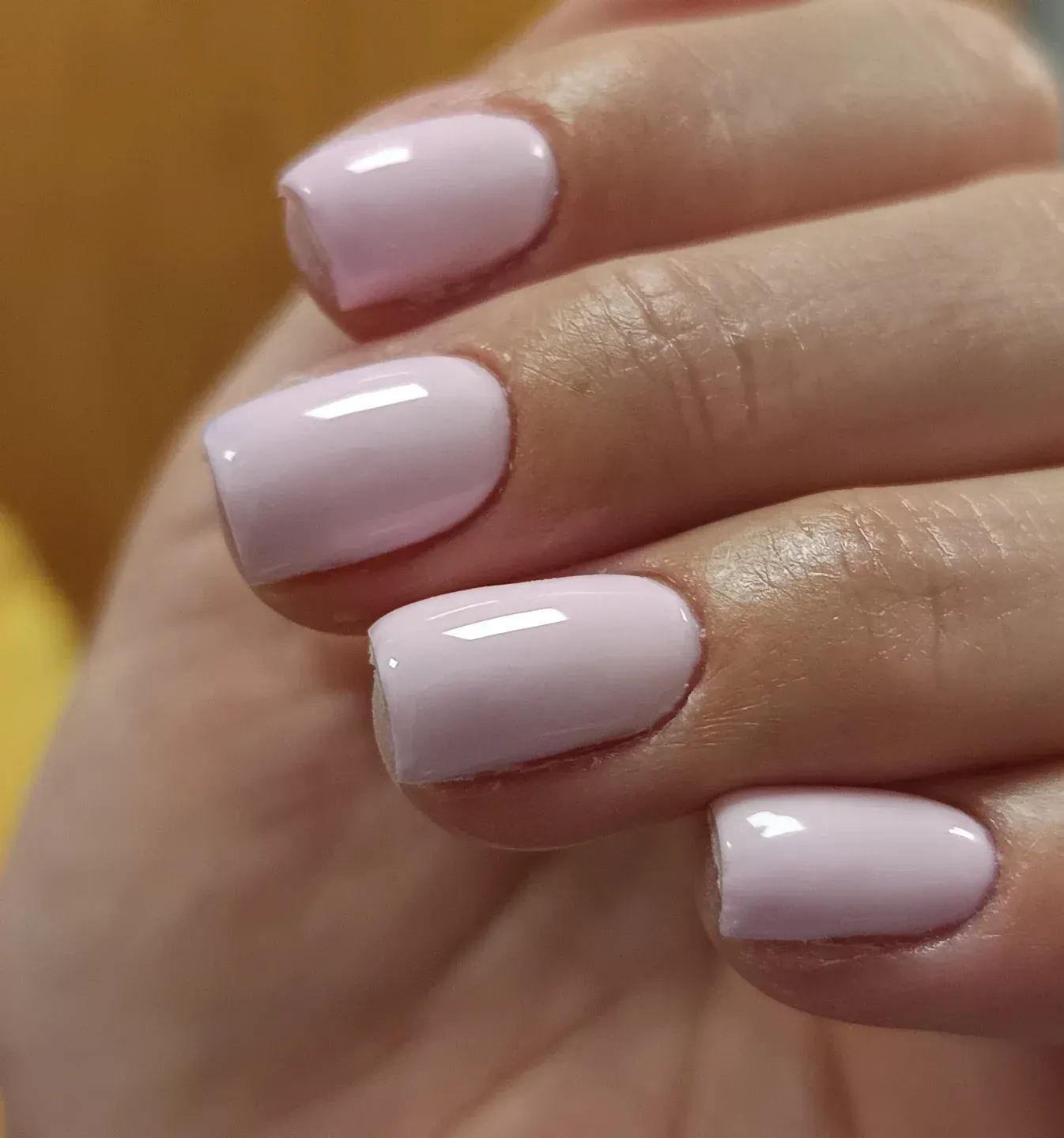 Primer plano de una mano con uñas pintadas de color rosa pálido brillante.