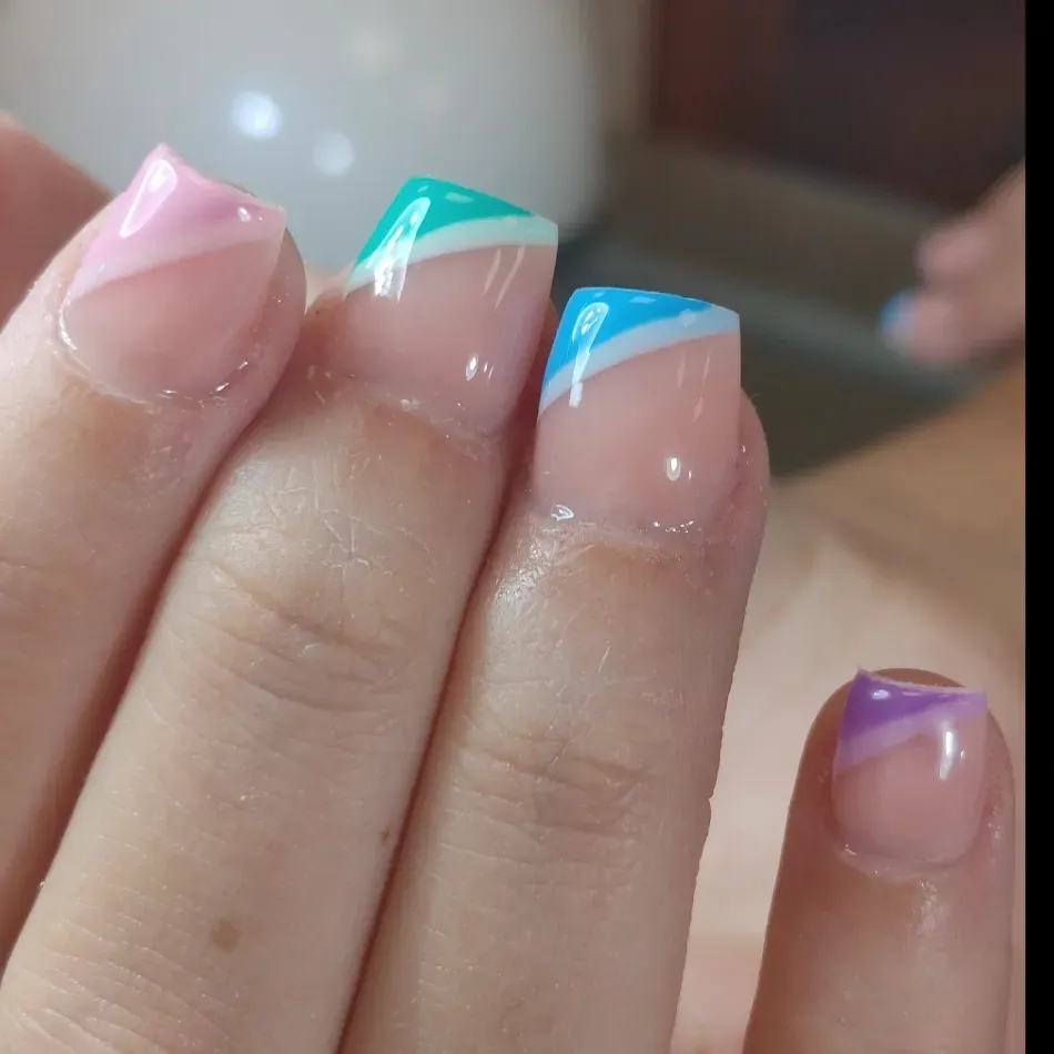 Primer plano de uñas manicuradas con puntas francesas en tonos rosa pastel, verde azulado, azul y morado.