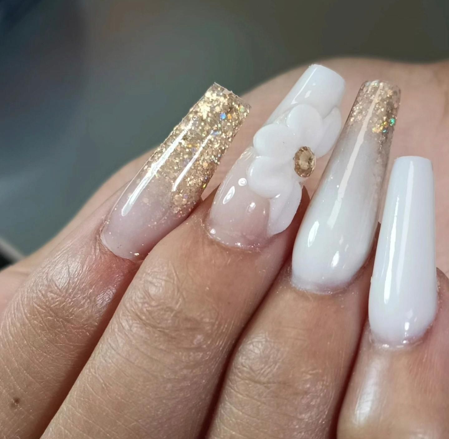 Uñas acrílicas largas blancas y color nude con purpurina dorada y detalles florales.