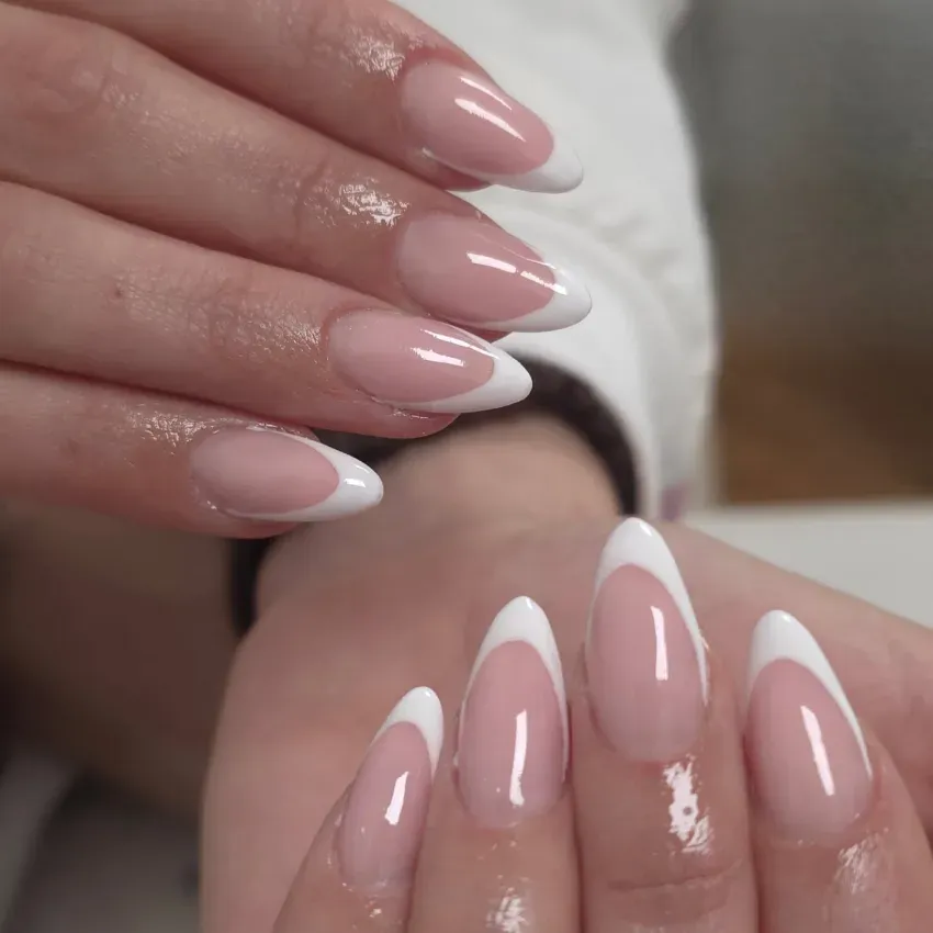 Manos con manicura francesa rosa nude y puntas blancas brillantes.