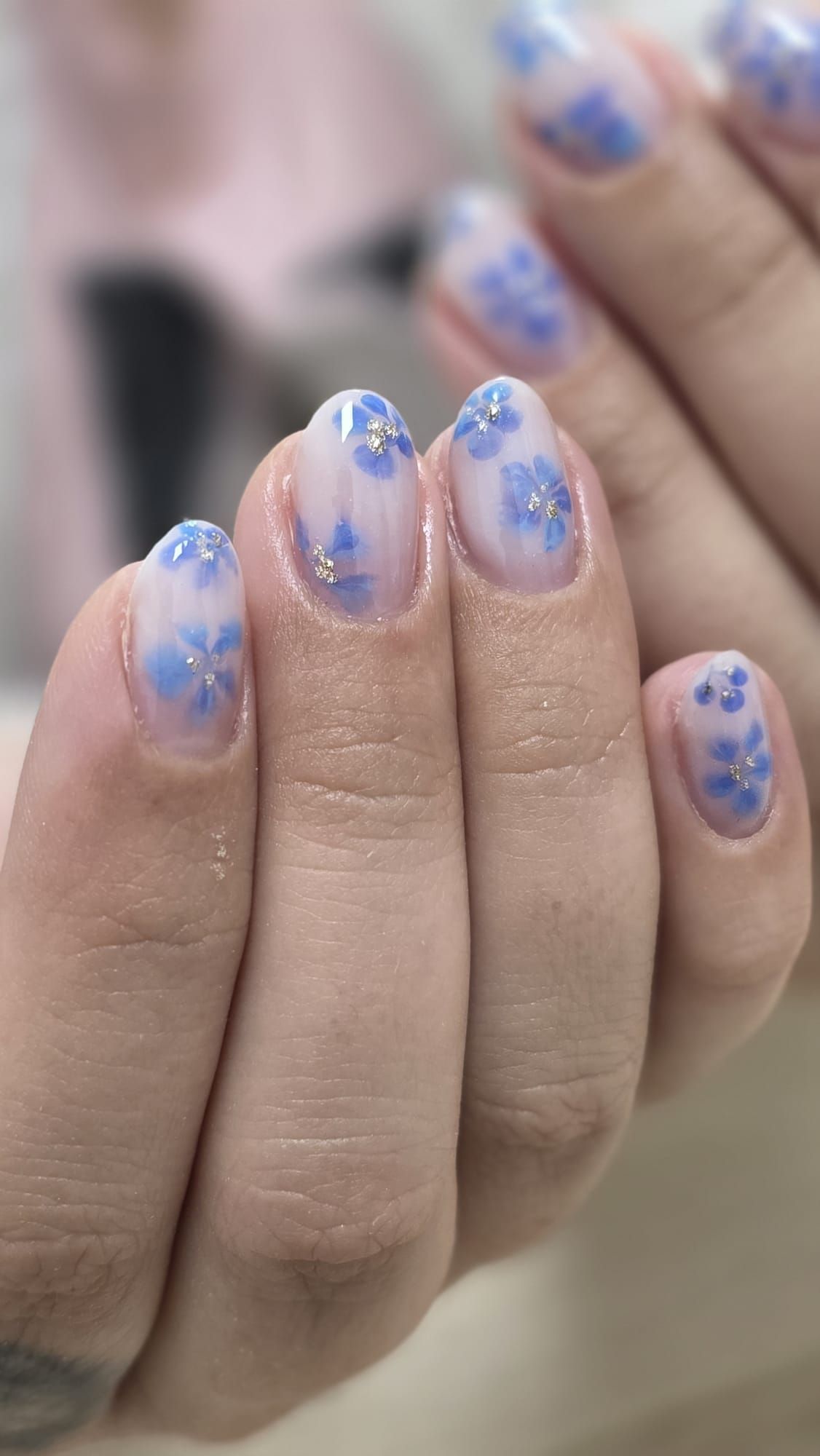 Primer plano de una mano con uñas decoradas con motivos florales azules y blancos sobre uñas naturales.