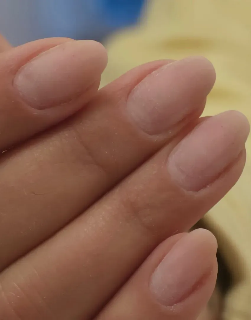 Primer plano de dedos cuidadosamente manicurados con uñas de color rosa pálido sobre un fondo amarillo suave.