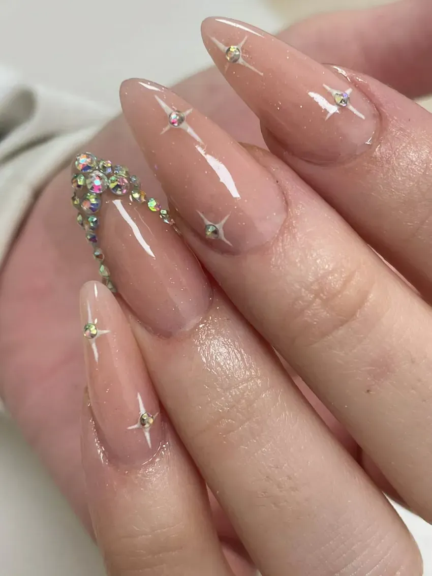 Primer plano de uñas pintadas en color rosa nude con detalles de estrellas plateadas y una uña con pedrería brillante.