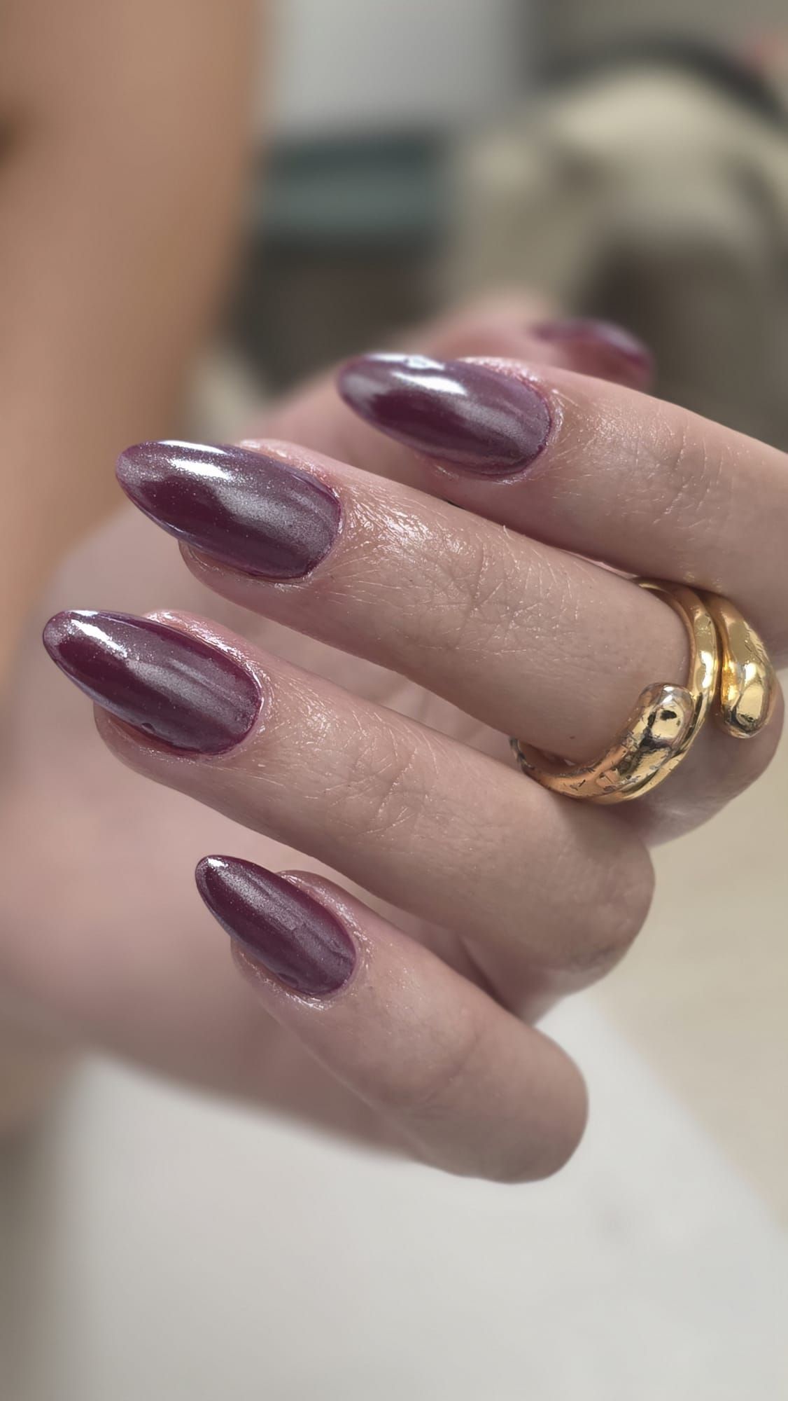 Mano con uñas largas y brillantes de color morado y anillos de oro.