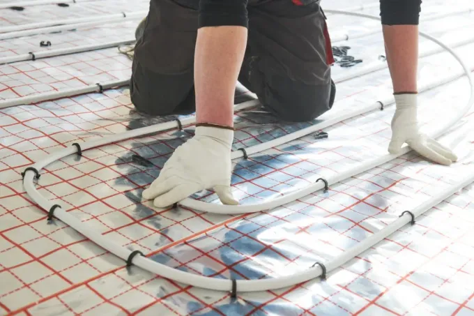 Persona instalando tubos de calefacción por suelo radiante sobre una superficie reflectante, con guantes.