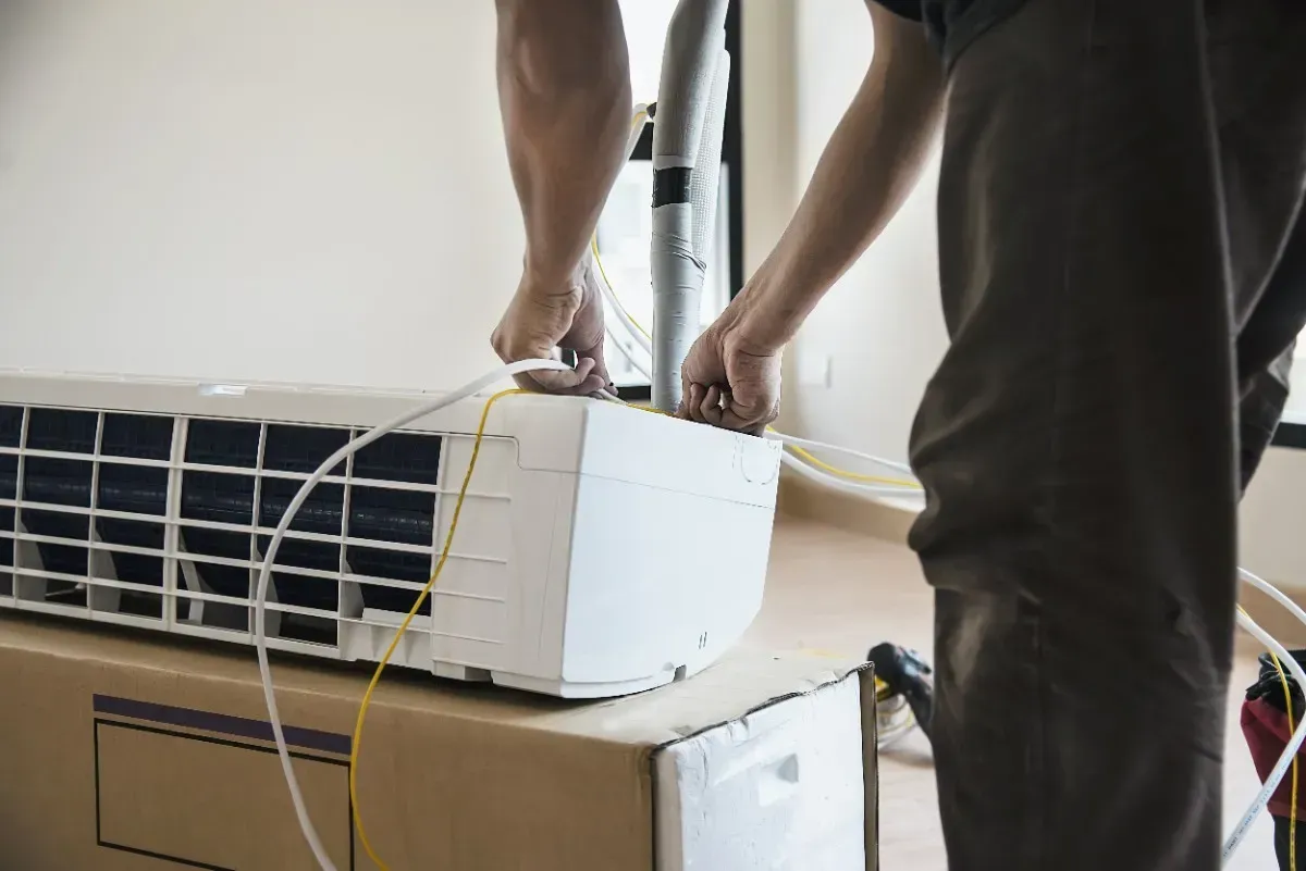 Persona instalando una unidad de aire acondicionado en el interior, conectando cables.