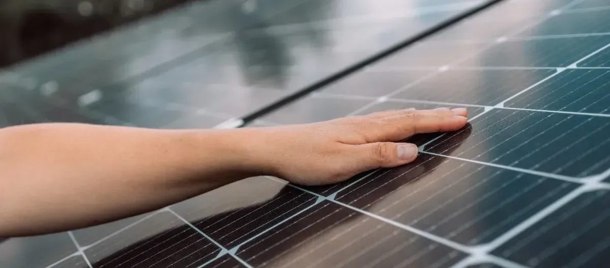 Mano tocando un panel solar, con una vista de cerca de las celdas.