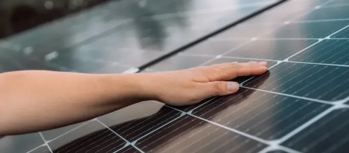 Mano tocando un panel solar, con una vista de cerca de las celdas.