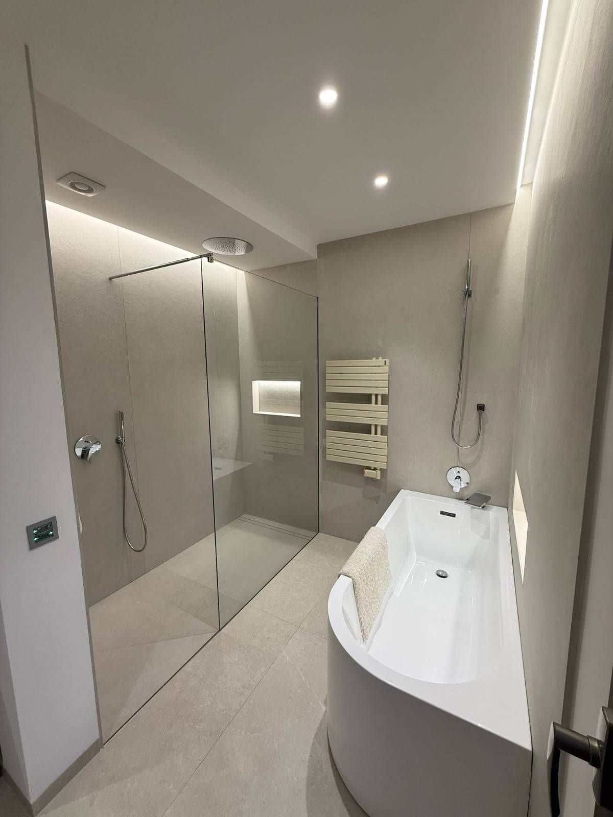 Baño moderno en tonos neutros que incluye una cabina de ducha de vidrio y una bañera profunda blanca.