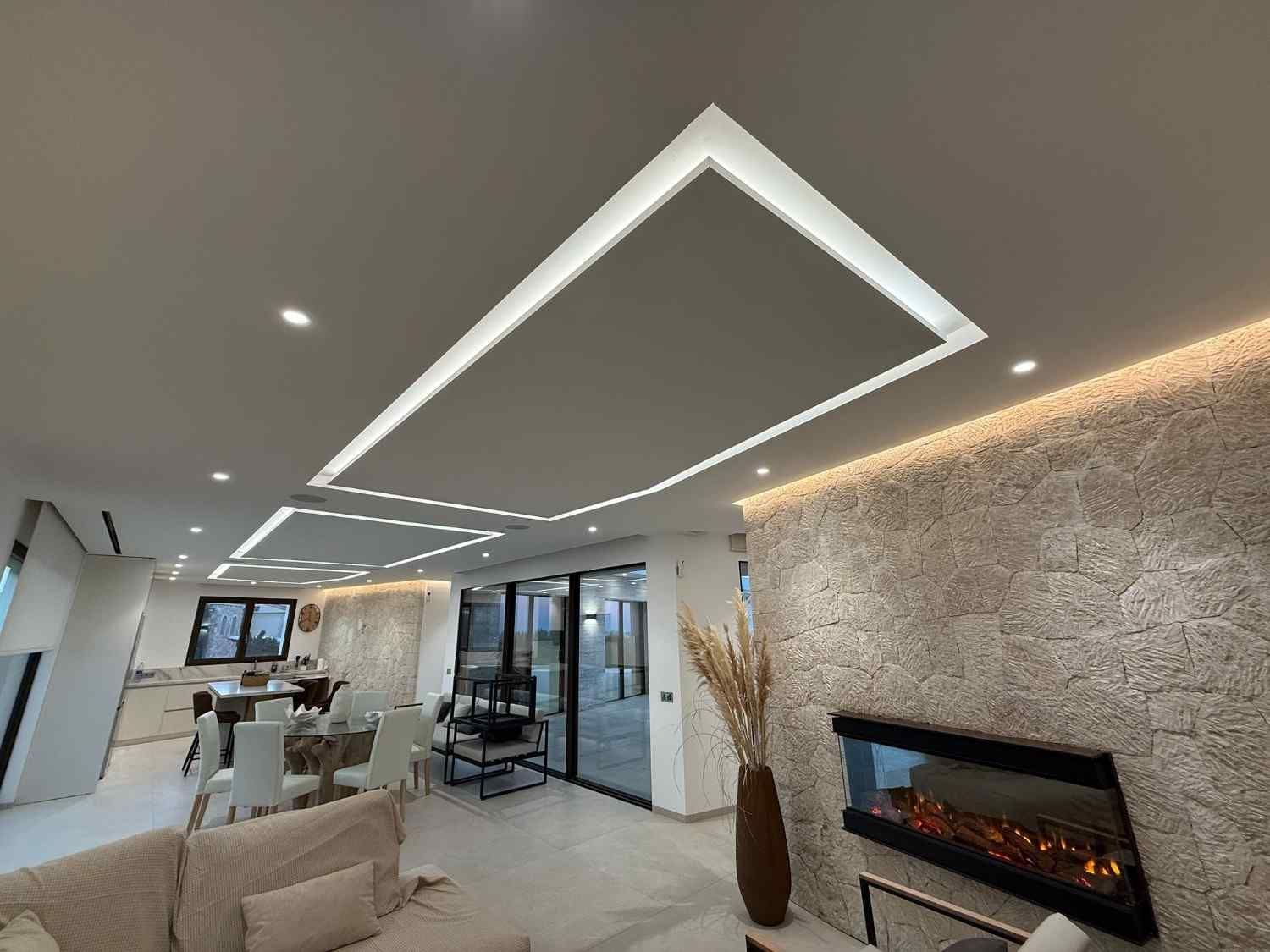 Moderna sala de estar con techo artesonado, iluminación LED empotrada, pared de piedra texturizada con chimenea y área de comedor.