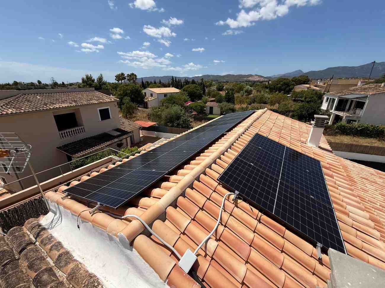 Paneles solares instalados en un techo de tejas de terracota bajo un cielo soleado y despejado.