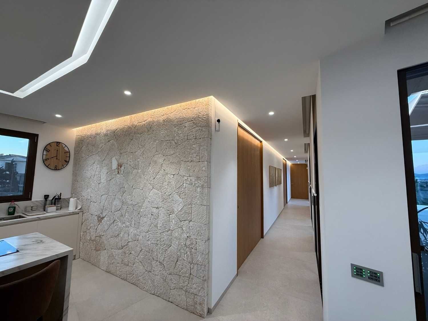 Interior moderno con una pared de piedra texturizada, iluminación LED oculta, puertas de madera y un pasillo que conduce a otras habitaciones.