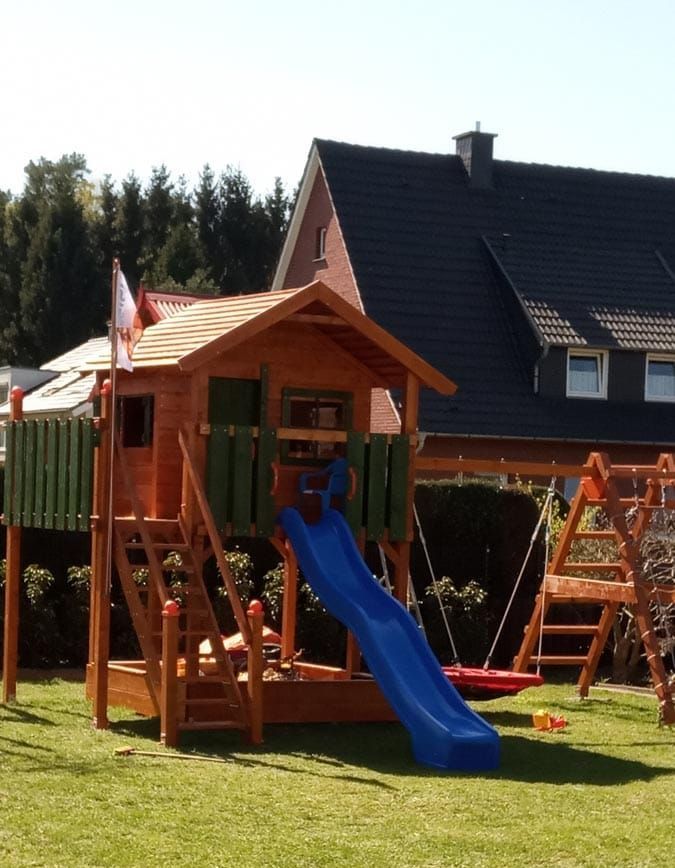 Ein Holzspielhaus mit blauer Rutsche und Schaukeln