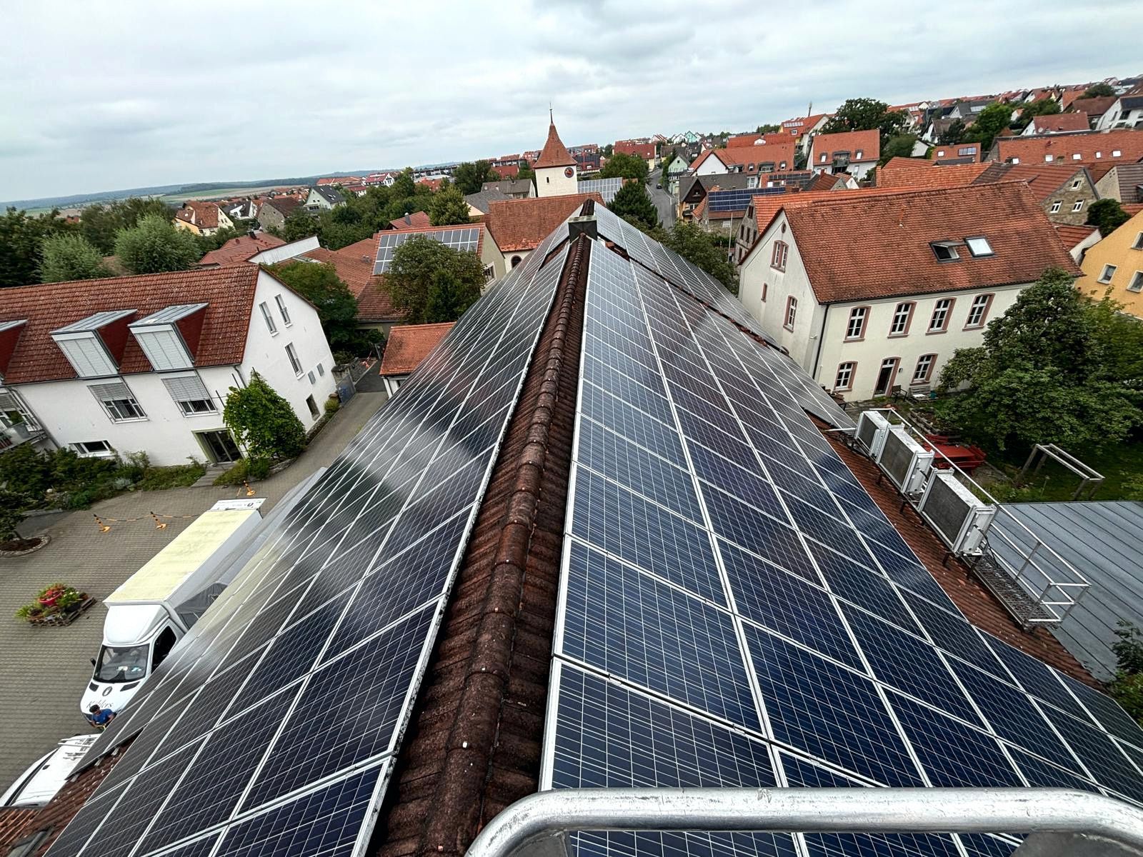 Solarpaneele auf den Dächern erstrecken sich unter bewölktem Himmel in Richtung der rotgedeckten Skyline einer Stadt.