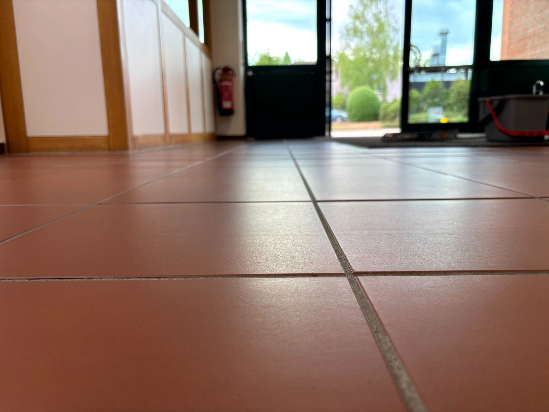 Ansicht von unten auf einen gefliesten Innenboden in der Nähe einer offenen Tür mit hellem Tageslicht draußen.
