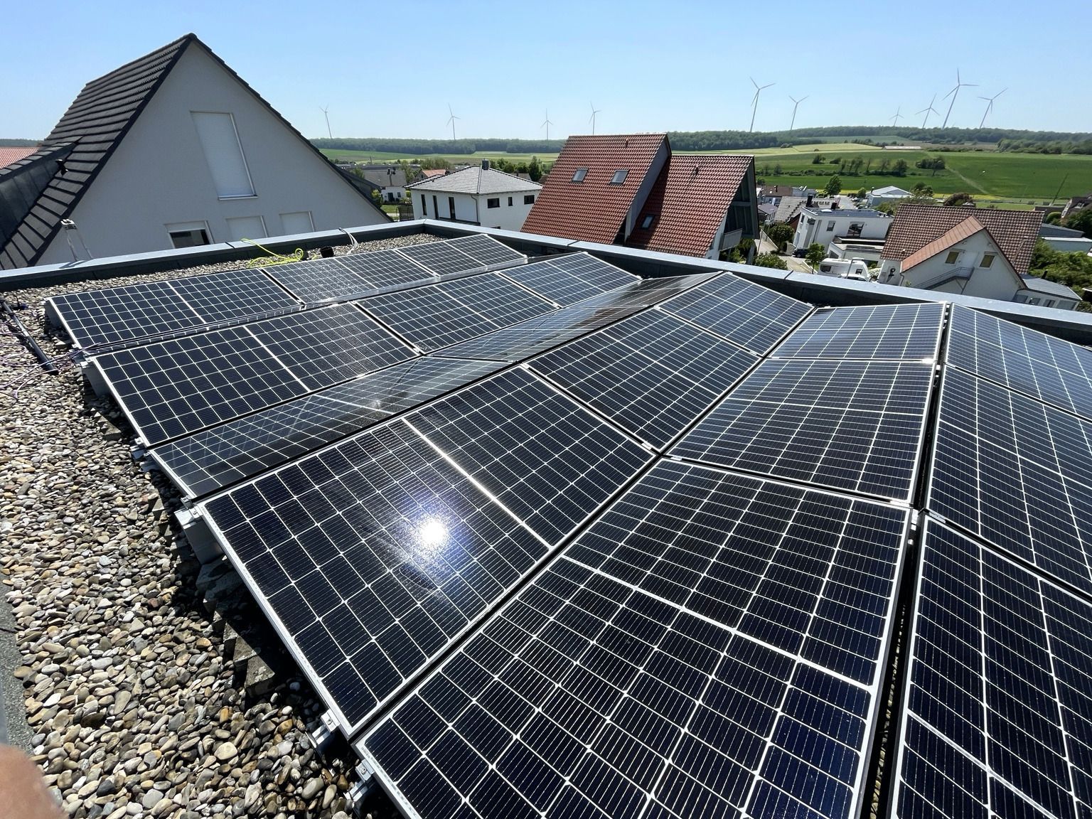 Auf einem Kiesdach installierte Solarpaneele, im Hintergrund Häuser und eine ländliche Landschaft.