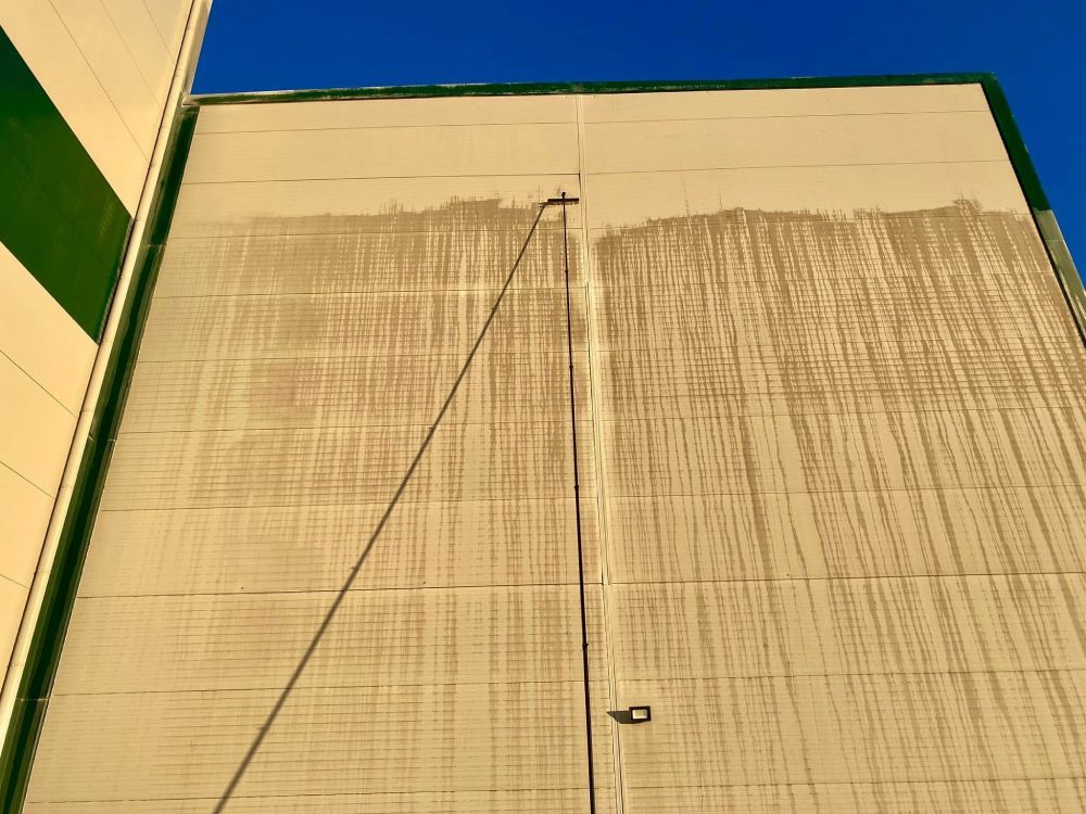 Eine hohe, beige Gebäudewand mit grünen Zierelementen und ein Kabel, das sich diagonal nach oben gegen den blauen Himmel spannt